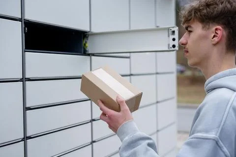 Young man using parcel locker with cardboard box Stock Photos