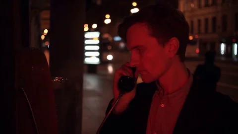 Young man using payphone at night in city srteet. Car city traffic at background Stock Footage 80009247
