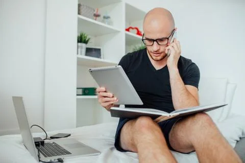 Young man is using pc tablet and talking by the phone with notepad on his kne Stock Photos