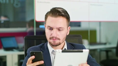 Young Man Using a Phone and a Tablet in the Office Stock Footage 84783003