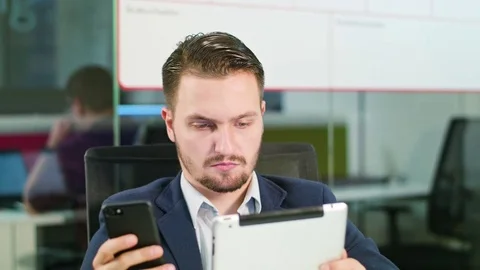 Young Man Using a Phone and a Tablet in the Office Stock Footage 84783463