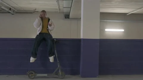 Young man using phone and laptop, sitting on his electric scooter in parkin.. Stock Footage 300437373