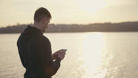 Young man using phone near lake Video stock 74312865