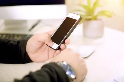 A young man is Using a phone with one hand while working on a desktop Stock Photos