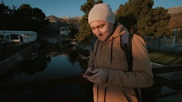 Young man using  phone in a park with palms in the autumn or winter time Video stock 85679426