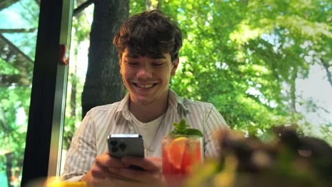 Young man using phone sitting in restaurant.Smiling man holding phone and on Stock Footage 202480043