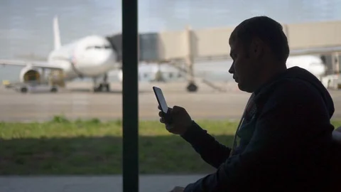 Young man using phone, watch screen of gadget, sitting on chair in airport room. Video stock 114000015