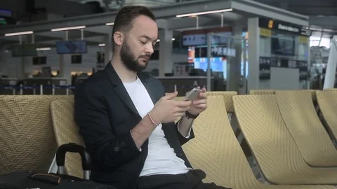 Young man is using phone while sitting in airport building. Video stock 85330501