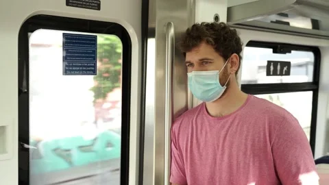 Young man using public transportation stands inside of a train wearing a surg Stockbeeldmateriaal 133062839