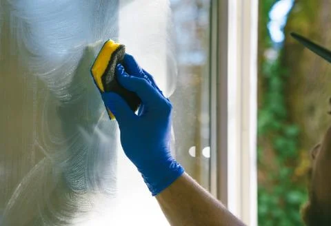 Young man is using a rag and squeegee while cleaning windows. Stock Photos