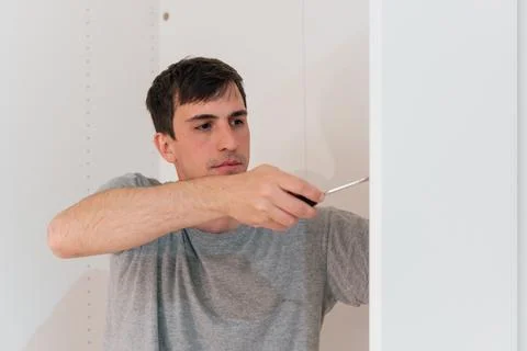 Young man using a screwdriver to assemble a closet at home Stock Photos