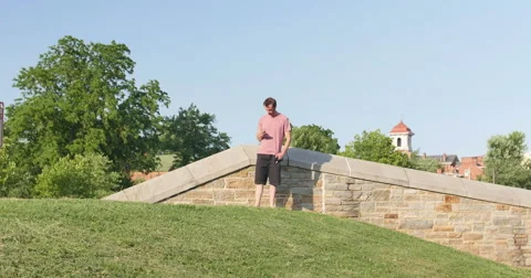 Young Man Using Smart Phone at Park with Blue Sky Trees Wide, 4K Stock Footage 65117011