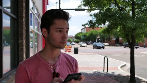 Young man using a smart phone by a busy down town street Stock Footage 76507303