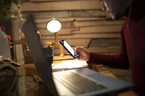 Young man using smart phone at laptop in home office Stock Photos