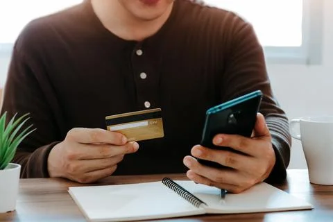 Young man using smart phone and credit card for shopping online in coffee sho Stock Photos