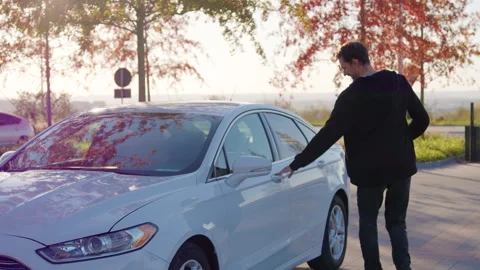Young man using a smartphone to access carsharing service, standing beside a Stock Footage 317702901