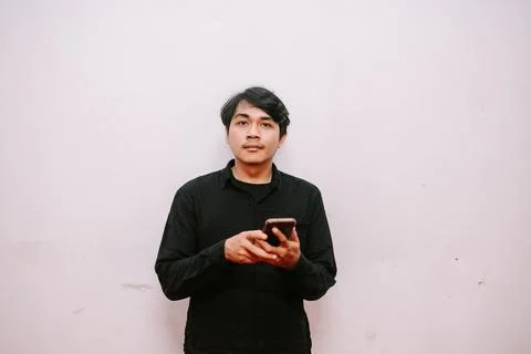 Young man using smartphone against a plain wall in a casual setting Foto stock