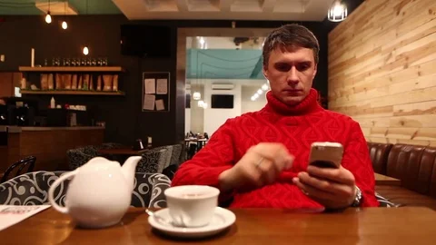 Young man using smartphone and drinking tee in cafe Vídeo Stock 71835384