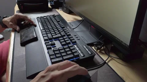 Young Man Using Smartphone and Typing on Keyboard at Computer Stock Footage 131437476