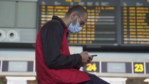Young man using smartphone and sitting on suitcase by airport panel Stock Footage 169937116