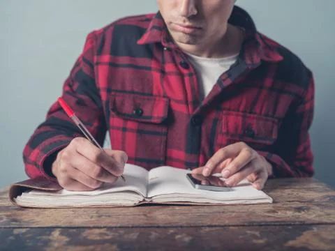 Young man using smartphone and taking notes Stock Photos