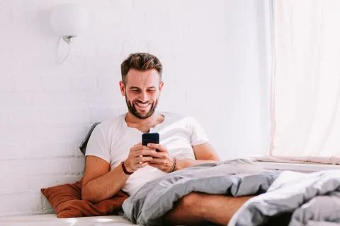 Young man using smartphone in the bed in the morning Stock Photos
