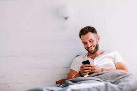Young man using smartphone in the bed in the morning Stock Photos