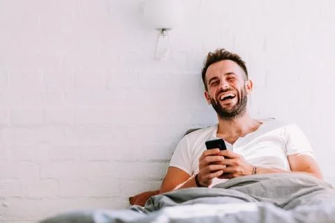 Young man using smartphone in the bed in the morning Stock Photos