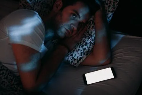Young man using smartphone in bed at night Stock Photos