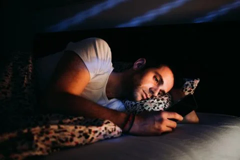Young man using smartphone in bed at night Stock Photos