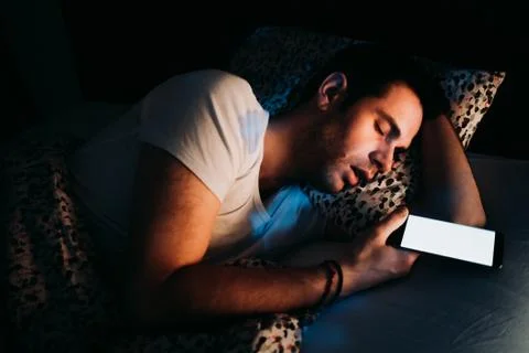 Young man using smartphone in bed at night Stock Photos