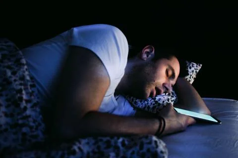 Young man using smartphone in bed at night Stock Photos