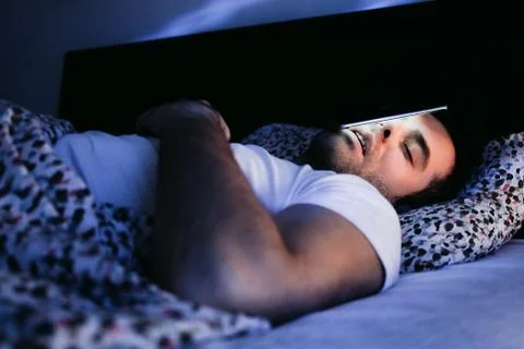Young man using smartphone in bed at night Stock Photos