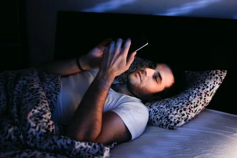 Young man using smartphone in bed at night Stock Photos