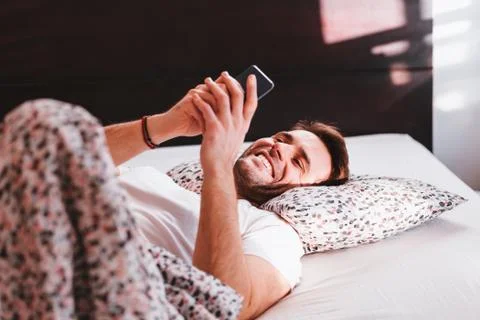 Young man using smartphone in bed in the morning Stock Photos