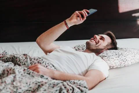 Young man using smartphone in bed in the morning Stock Photos