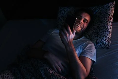 Young man using smartphone in bed at night Stock Photos