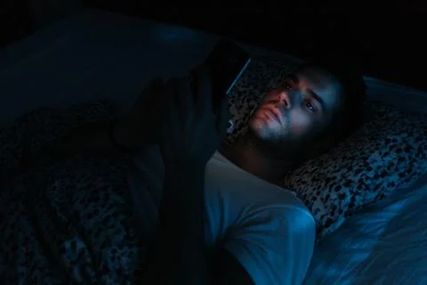 Young man using smartphone in bed at night Stock Photos