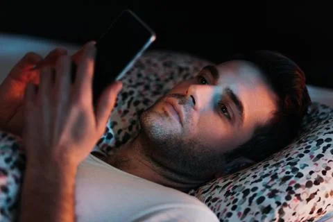 Young man using smartphone in bed at night Stock Photos