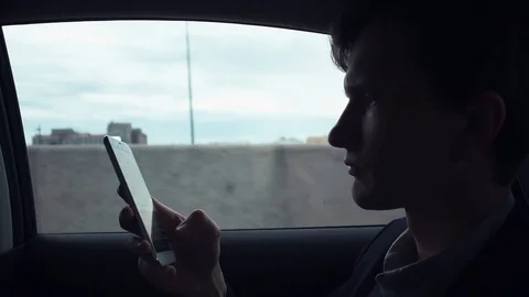 Young man using smartphone in car checking mails, chats or news online Stock Footage 80009146