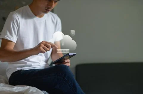Young man using smartphone with cloud computing icon indoors in casual settin Fotos Stock