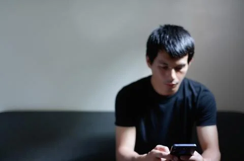 Young Man Using Smartphone in Dimly Lit Room, Casual Pose Stock Photos