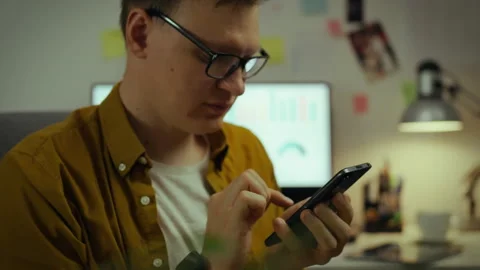 Young man using smartphone in a home office with computer and workspace clut Stock Footage 331297804