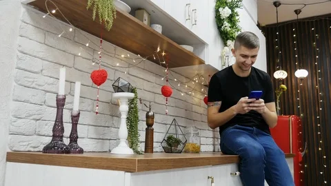 Young man using smartphone in modern kitchen, chatting with friends, surfing Video stock 103033746