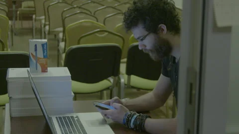 Young man using smartphone next to laptop in empty hall Stock Footage 341864094