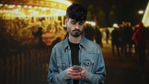 Young man using smartphone at night fair looks thoughtful with bright light.. Stock Footage 310641395