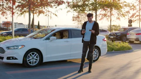 Young man using smartphone for online payments while standing beside white car Stock Footage 317701890