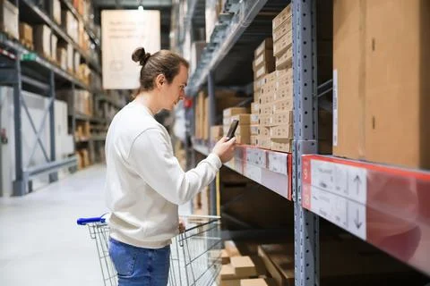 Young man using smartphone to scan product code in furniture warehouse stor.. Stock Photos