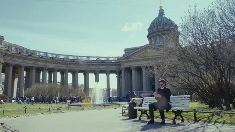 Young man using smartphone, sitting on bench near orthodox church. Sunny day Stock Footage 76049028