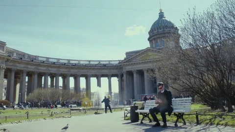 Young man using smartphone, sitting on bench near historical building. Sunny day Stock Footage 76049168